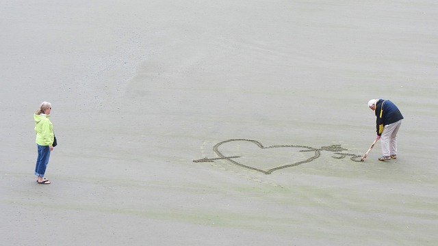 zamilovaný senior kreslí srdce do písku